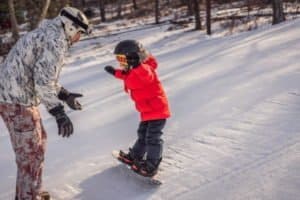 kleiner Junge bekommt Hilfe von Betreuer beim Snowboard