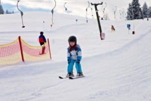 Adorable little boy with blue jacket and a helmet, skiing wintertime