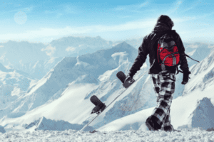 Jugendlicher trägt Snowboard mit Bergblick